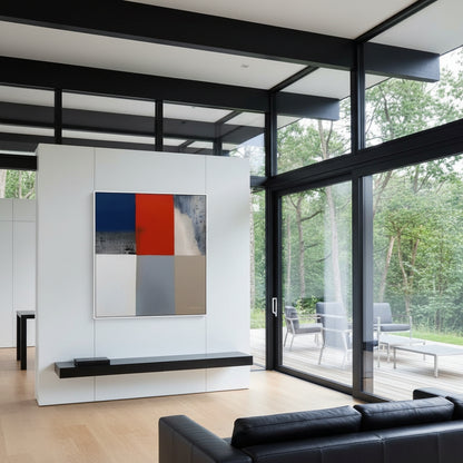 Modern living room with a black sofa, abstract art on the wall, and large glass windows overlooking trees.