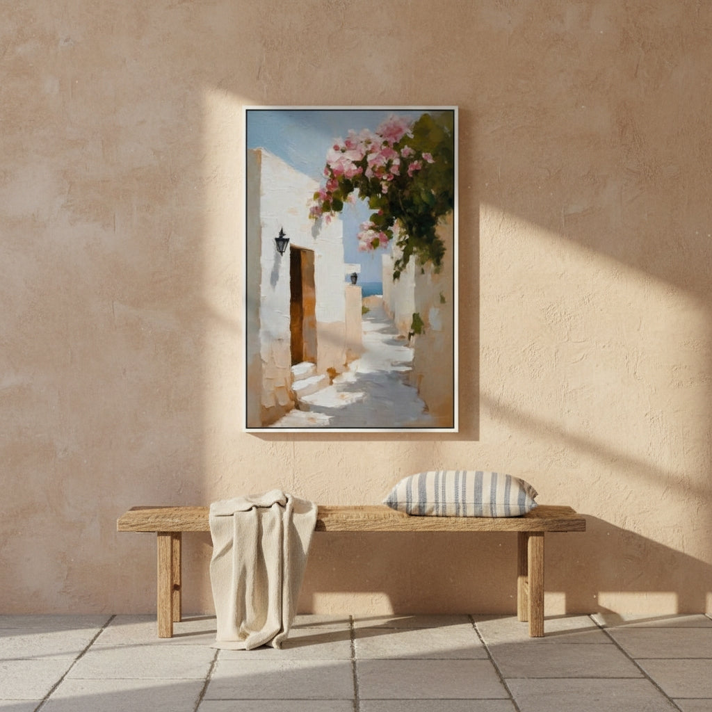 Framed artwork of a mediterranean alley scene with flowers on a beige wall above a wooden bench.