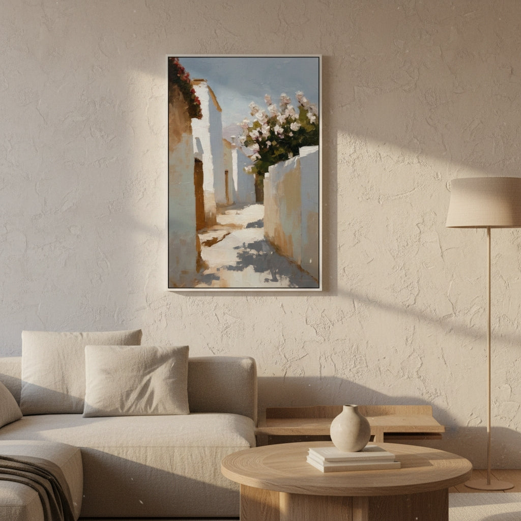 Framed artwork of a sunlit street scene with white buildings and flowers, hanging on a textured wall above a sofa.