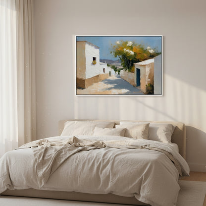 Framed artwork of a Mediterranean street scene above a bed in a bedroom.
