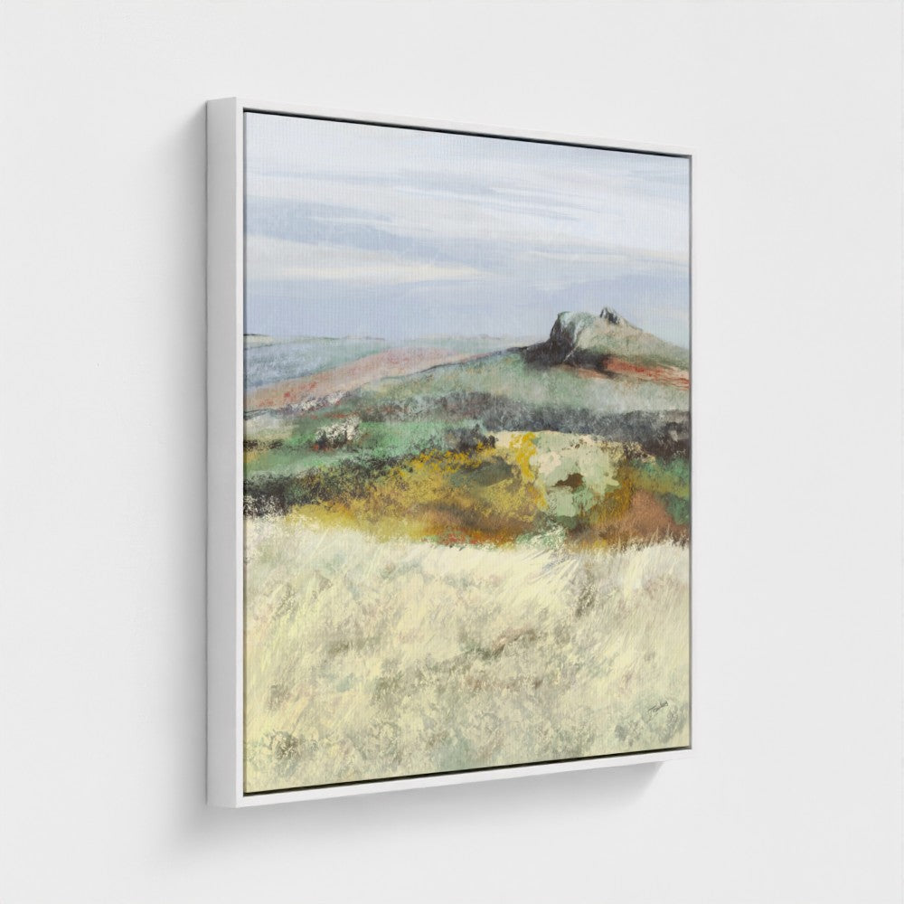 Framed landscape painting of a rural scene with fields and a distant hill on a white wall.
