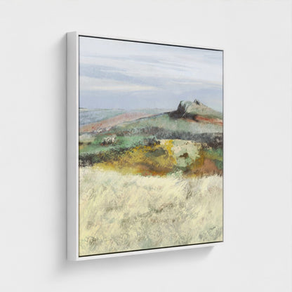 Framed landscape painting of a rural scene with fields and a distant hill on a white wall.